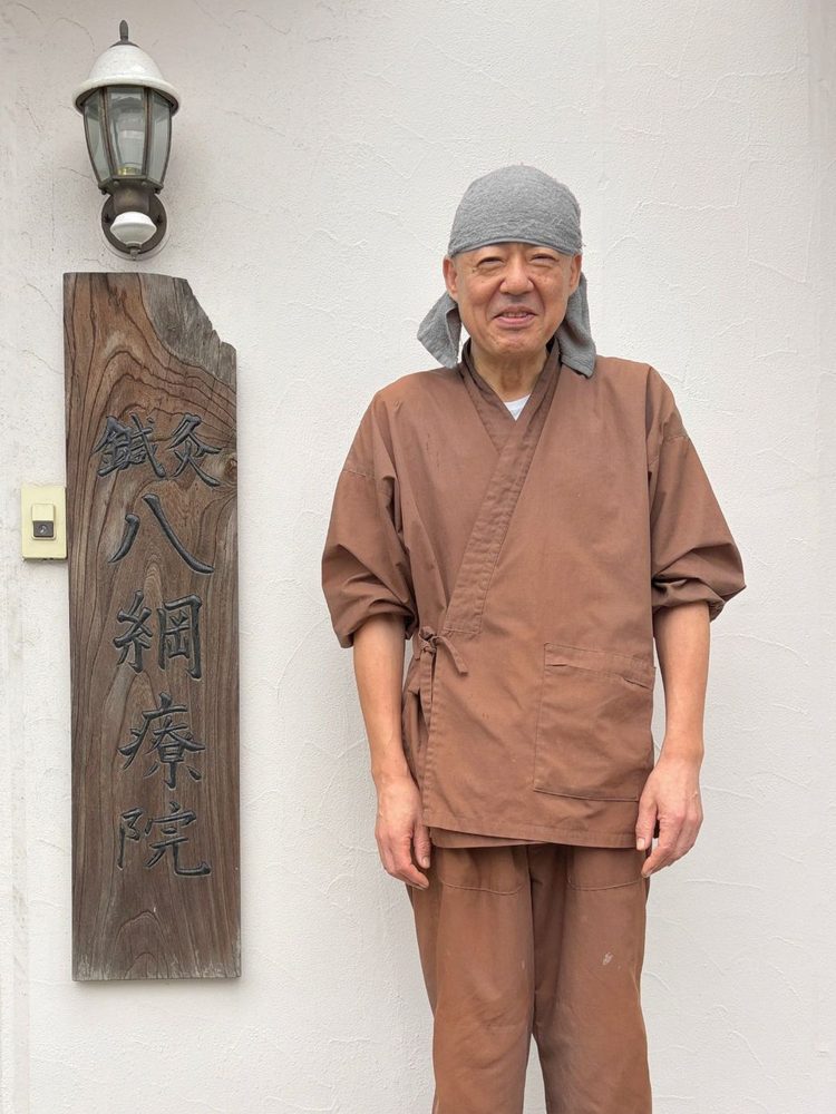 八綱療院の看板の前に立つ院長 柴田幸昌